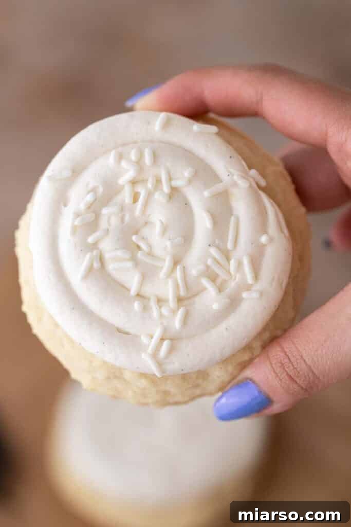 A hand holding a perfectly frosted Crumbl Nilla Bean Cupcake Cookie, ready to be enjoyed.