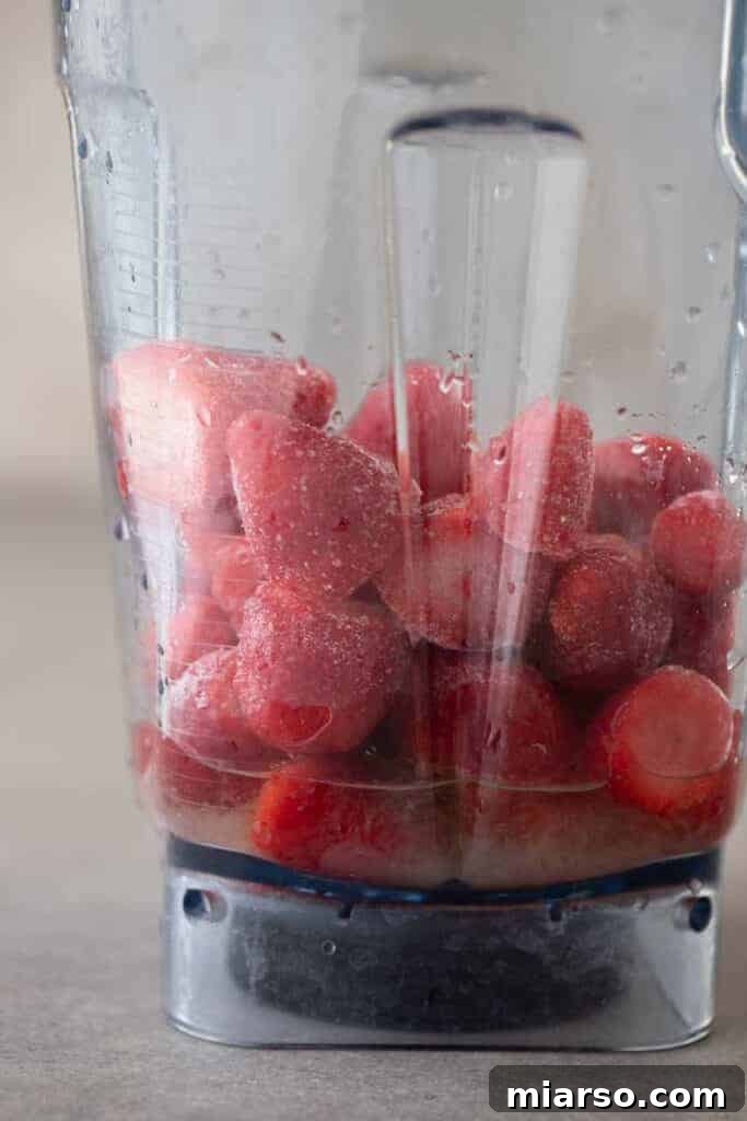 Frozen strawberries, lime juice, and agave syrup in a blender cup before blending.