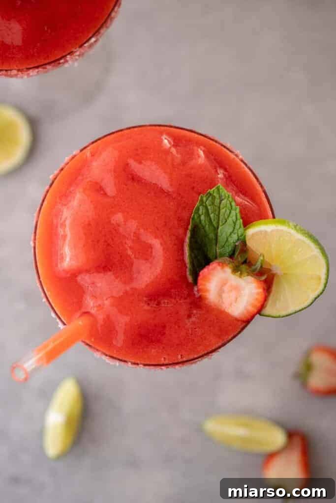 Overhead shot of two glasses of frozen strawberry margarita with lime and strawberry garnishes.