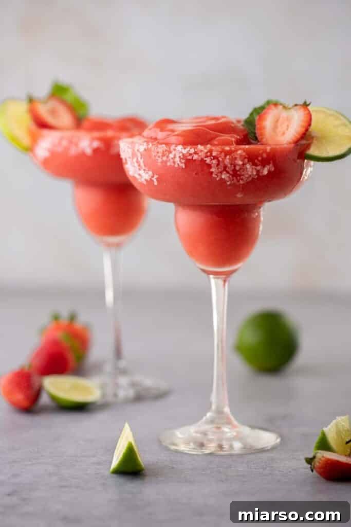 A perfectly blended frozen strawberry margarita in a salt-rimmed glass, garnished with a fresh lime wedge and strawberry.