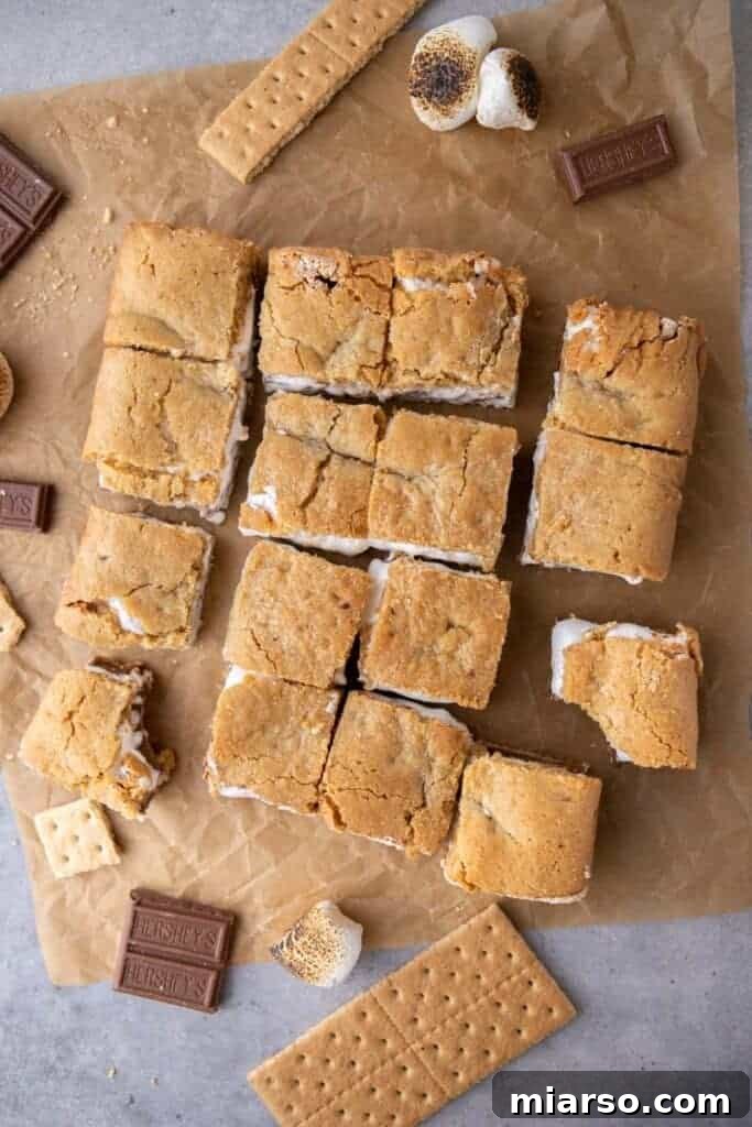 A stack of freshly sliced s'mores bars on a wooden cutting board, with the gooey layers visible.