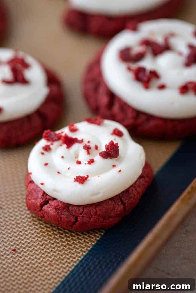 Crumbl red velvet cupcake cookies with cream cheese frosting and red velvet crumbs on top, displayed beautifully on a white background.