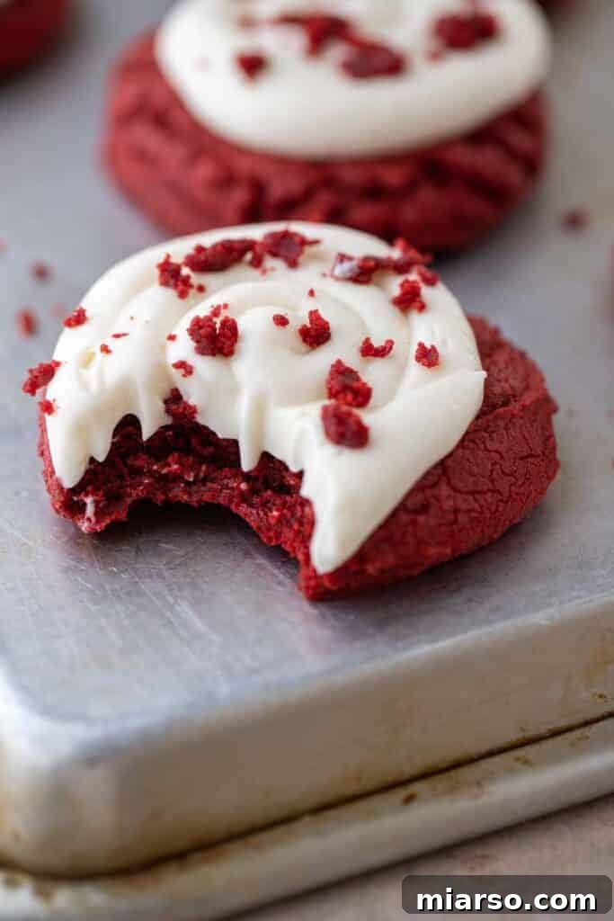 A red velvet cupcake cookie with a bite taken out, revealing its soft, plush interior and creamy frosting.