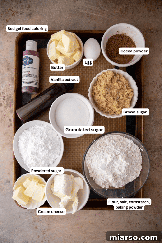 Various baking ingredients including butter, sugars, flour, cocoa powder, and red food coloring laid out on a kitchen counter, ready for baking.
