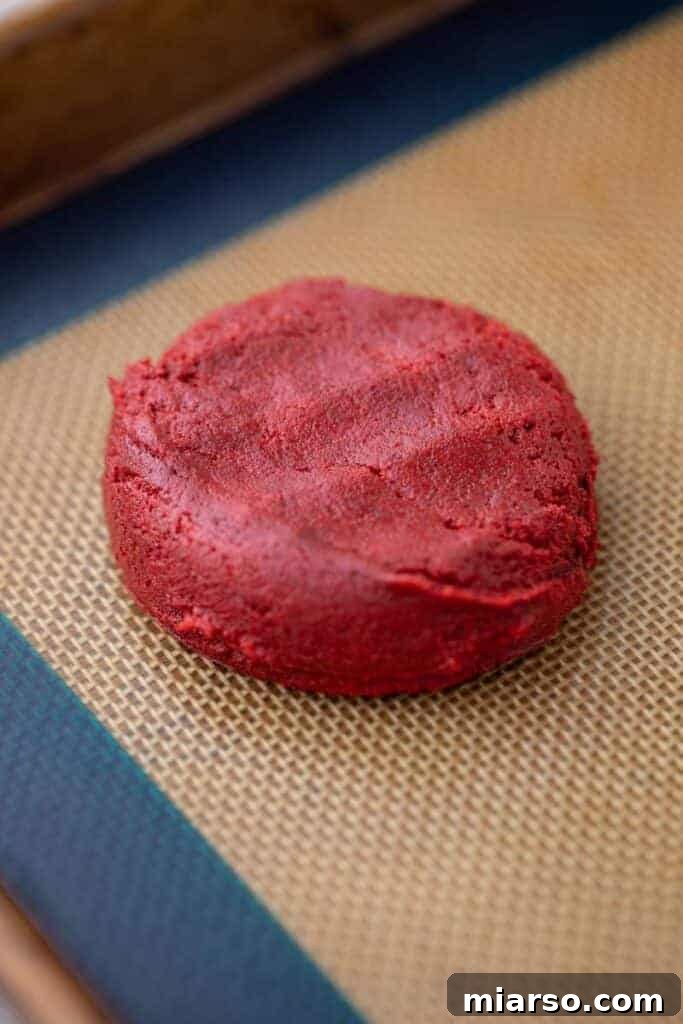 Crumbl red velvet cupcake cookie dough balls flattened on a baking pan, ready to go into the oven.