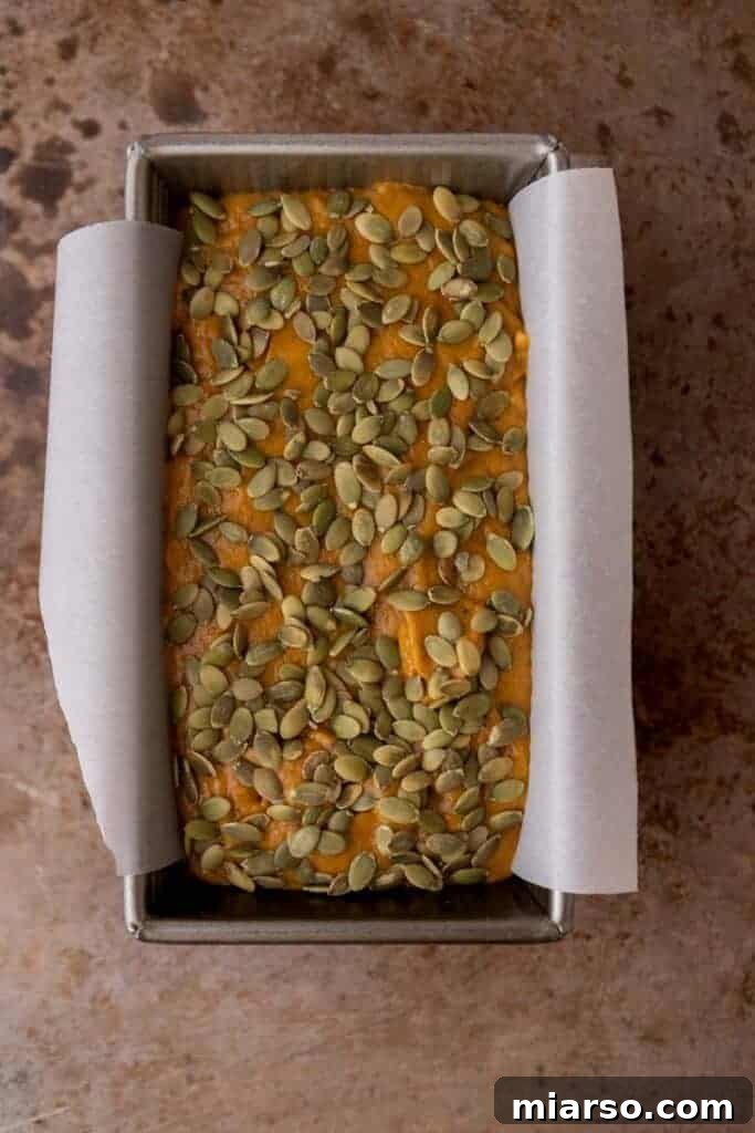 Pumpkin bread batter poured into a loaf pan, topped with pumpkin seeds.