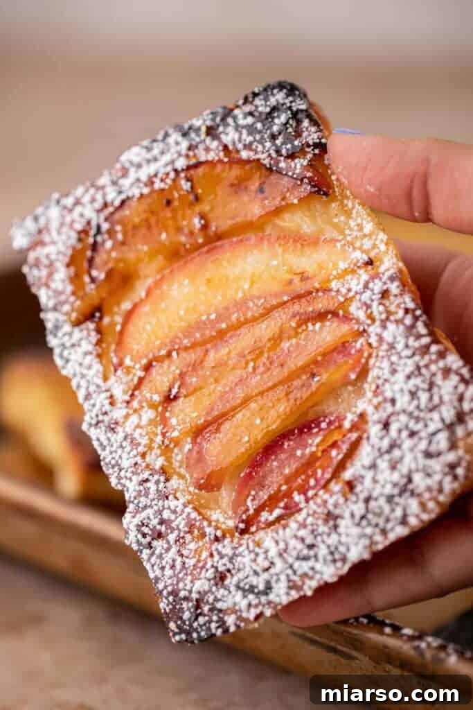 Hand holding golden brown upside down apple pastry with caramelized apples