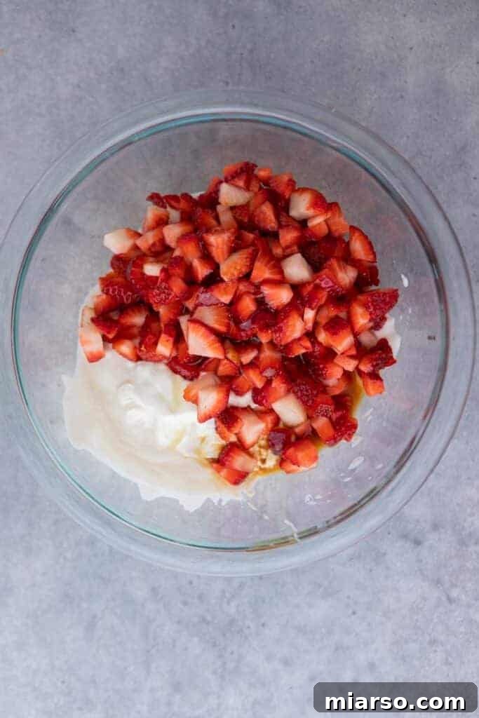 Diced strawberries and Greek yogurt in a mixing bowl, ready to be combined for yogurt clusters.