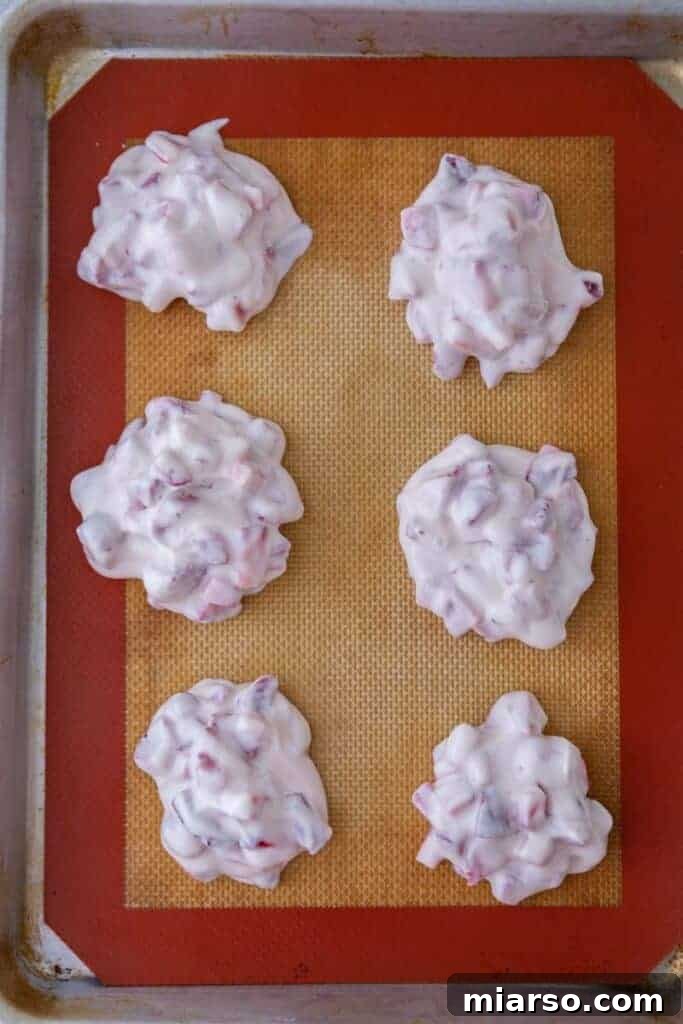 Portioned strawberry yogurt clusters arranged on a baking sheet, ready for freezing.