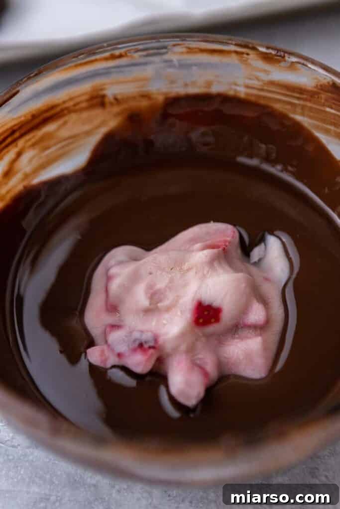 A frozen yogurt cluster being dipped into melted chocolate.