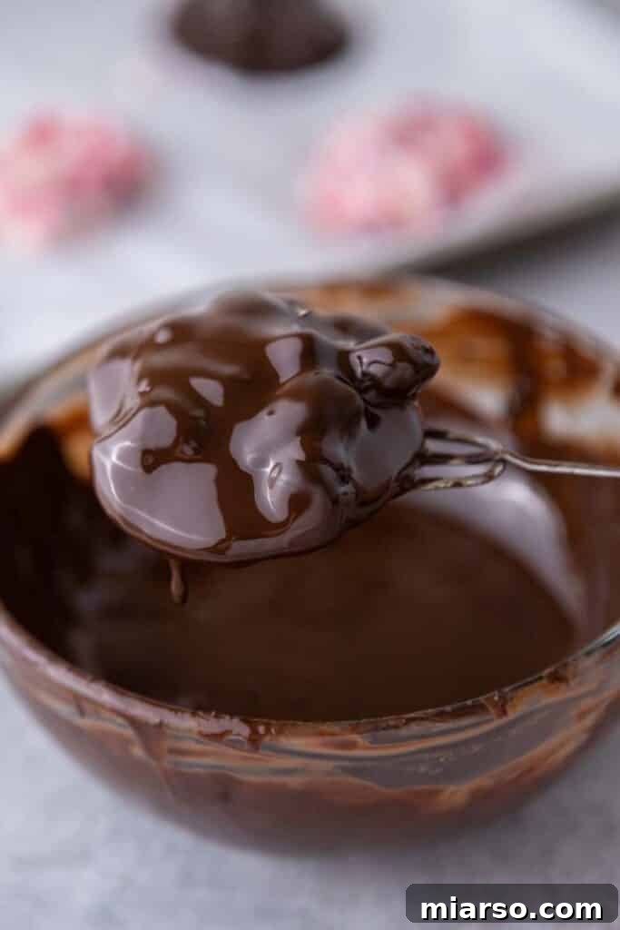 A yogurt cluster freshly dipped in chocolate, ready to be placed back on the baking sheet.