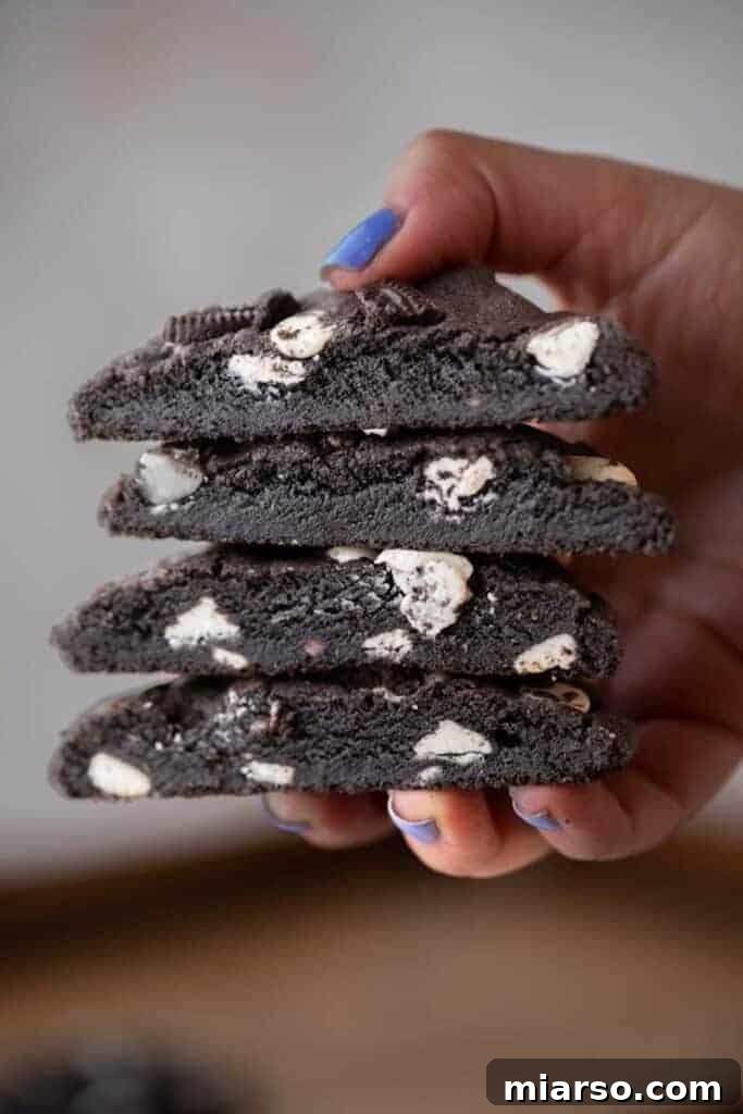 Crumbl's Chocolate Cookies & Cream Bliss 2 A hand holding a stack of freshly baked Crumbl Chocolate Cookies and Cream Cookies, showcasing their rich dark color and white chocolate chunks.