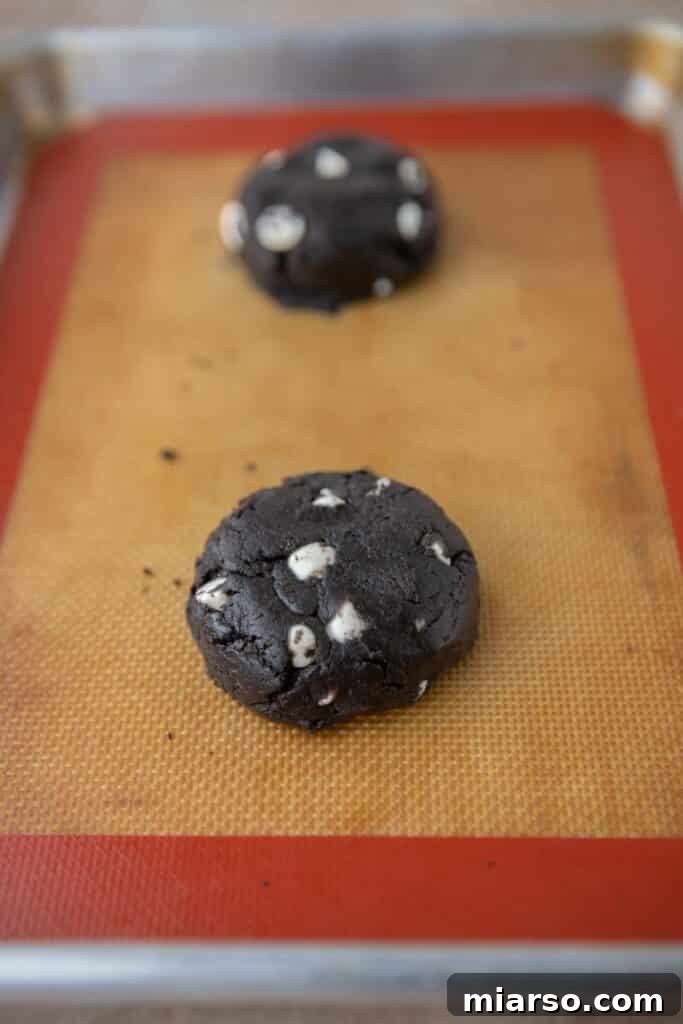 Crumbl's Chocolate Cookies & Cream Bliss 8 Scooped and flattened cookie dough balls on a parchment-lined baking sheet, prepared for oven.