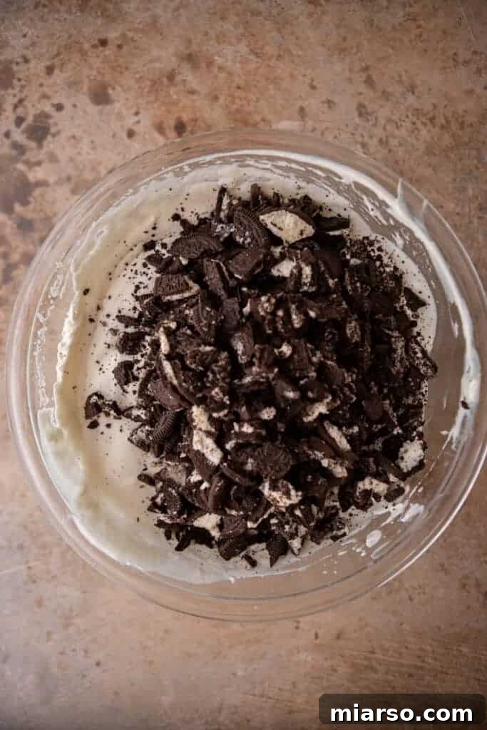 Simply Delicious No Churn Oreo Ice Cream 6 The creamy mixture of whipped cream, sweetened condensed milk, and vanilla extract, with chopped Oreo cookies gently folded in, creating the base for no-churn cookies and cream ice cream.