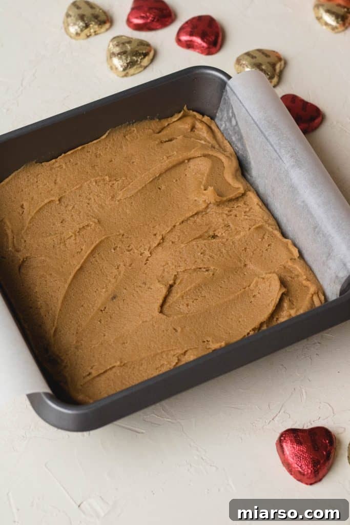 Pouring peanut butter blondie batter into a parchment-lined baking pan.