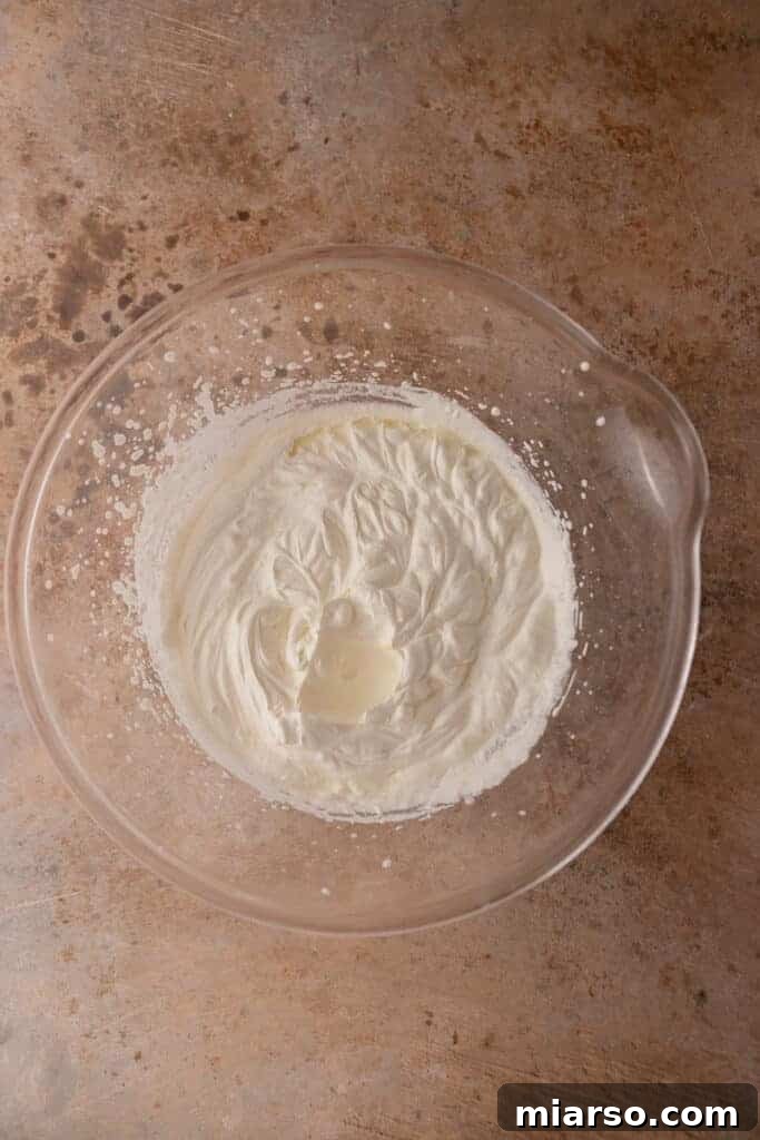 Close-up of fluffy, white whipped cream in a glass bowl, illustrating a key step in ice cream making.