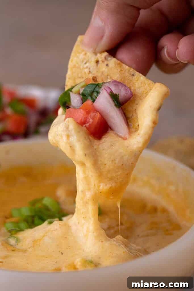 Crispy tortilla chip scooping creamy cottage cheese queso from a bowl