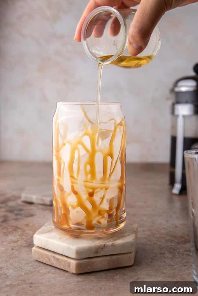 Quick 5-Minute Iced Caramel Coffee Perfection 5 Caramel syrup being poured into a tall glass filled with ice, illustrating the first step of the recipe.