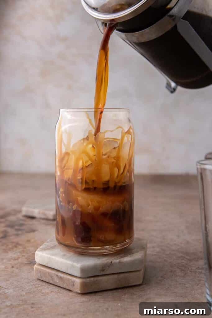 Quick 5-Minute Iced Caramel Coffee Perfection 6 Freshly brewed coffee being poured over ice in a tall glass, forming layers with the caramel.