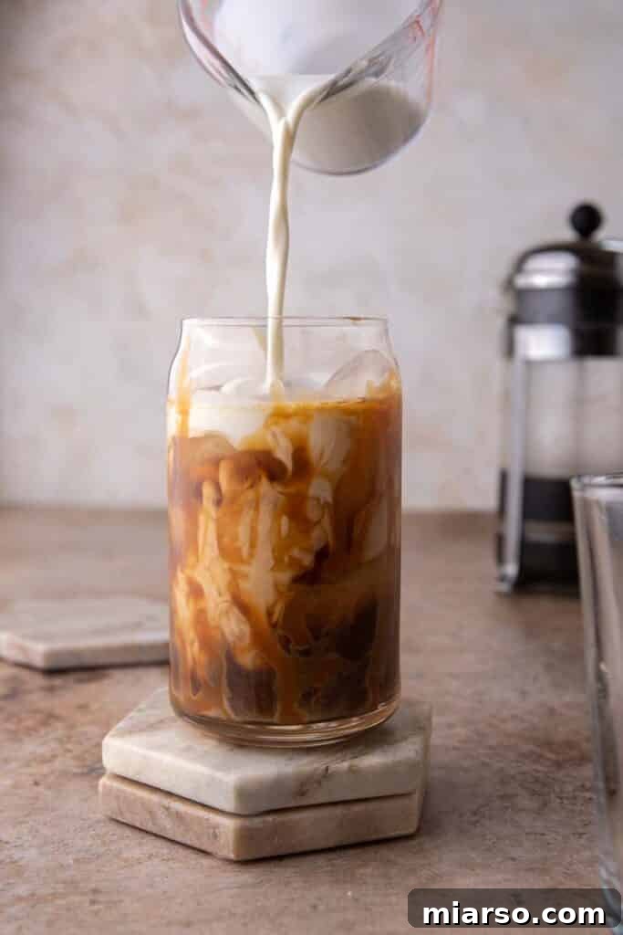 Quick 5-Minute Iced Caramel Coffee Perfection 7 Creamer being added to a glass of iced coffee, creating a swirl effect and adding richness.