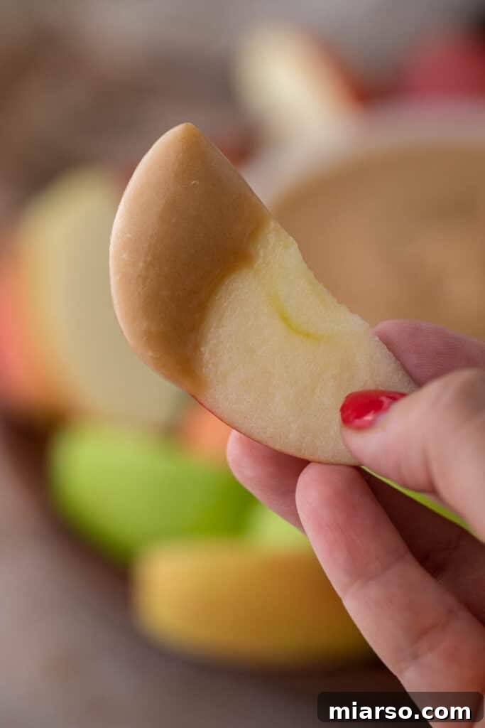 Crafting the Perfect Homemade Caramel Apple Dip 8 A hand holding a fresh apple slice generously coated in homemade caramel sauce.