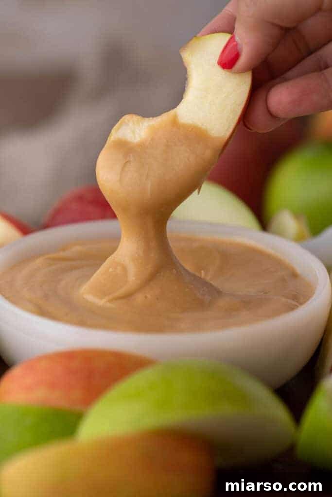 Crafting the Perfect Homemade Caramel Apple Dip 10 A single apple wedge perfectly dipped in a thick, golden caramel sauce, highlighting its gooey texture.