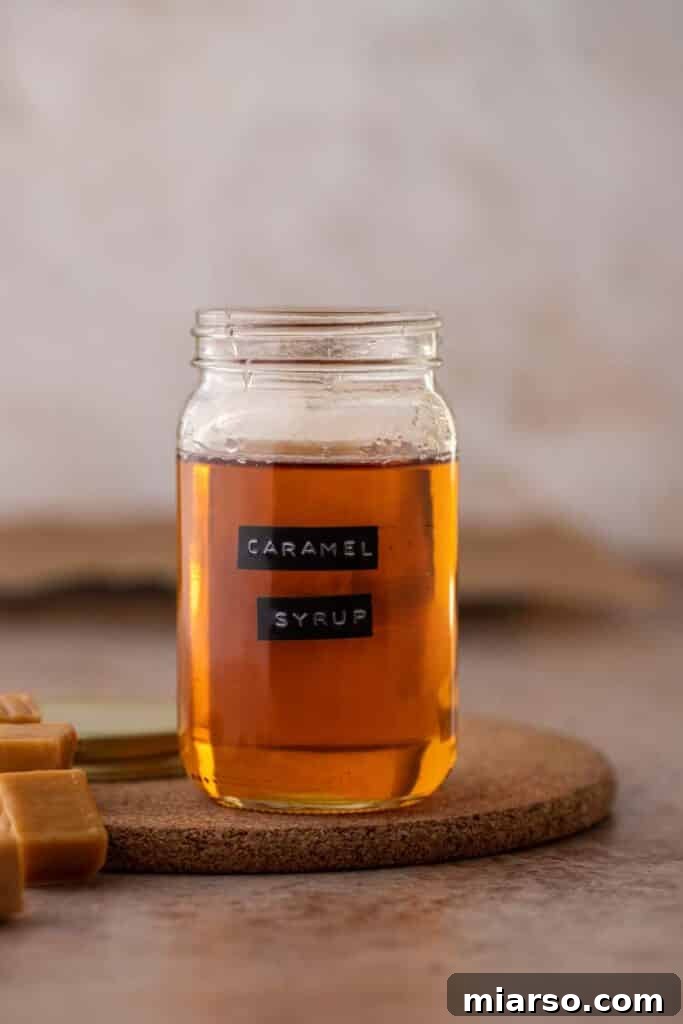 Homemade caramel syrup in a glass jar, next to a coffee cup. The best caramel syrup for coffee.