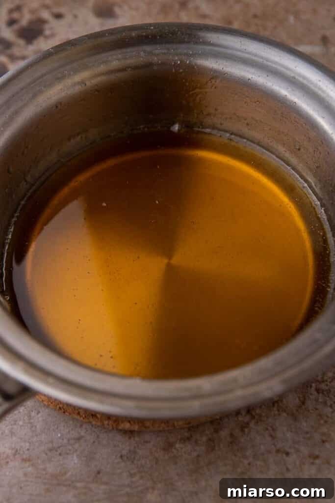 A stream of rich, golden caramel syrup being poured from a saucepan, highlighting its perfect consistency.