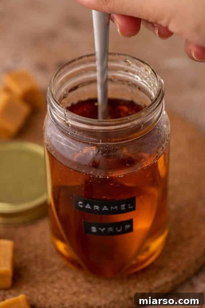 A full jar of homemade caramel syrup for coffee, with a spoon nearby, ready to be used.