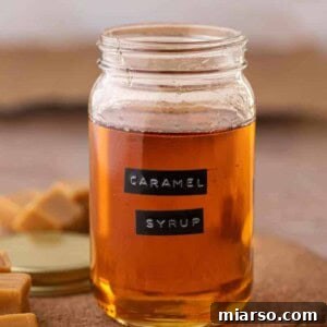 Homemade caramel syrup in a glass jar, next to a coffee cup. The best caramel syrup for coffee.