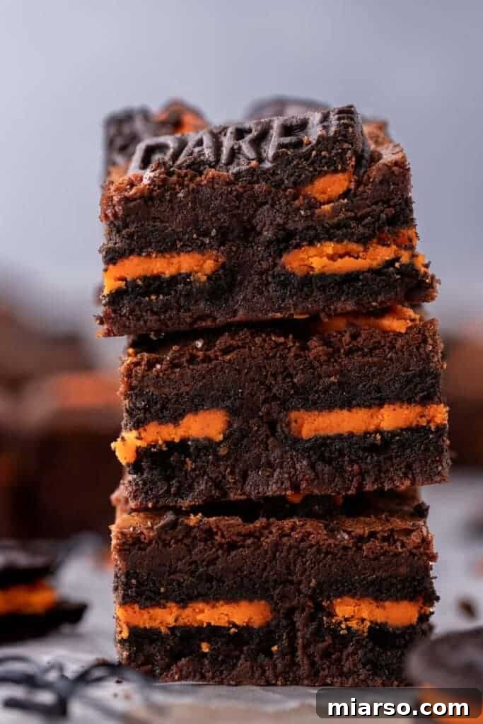 A stack of three rich, fudgy Halloween Oreo brownies with visible Oreo pieces, ready to be enjoyed.