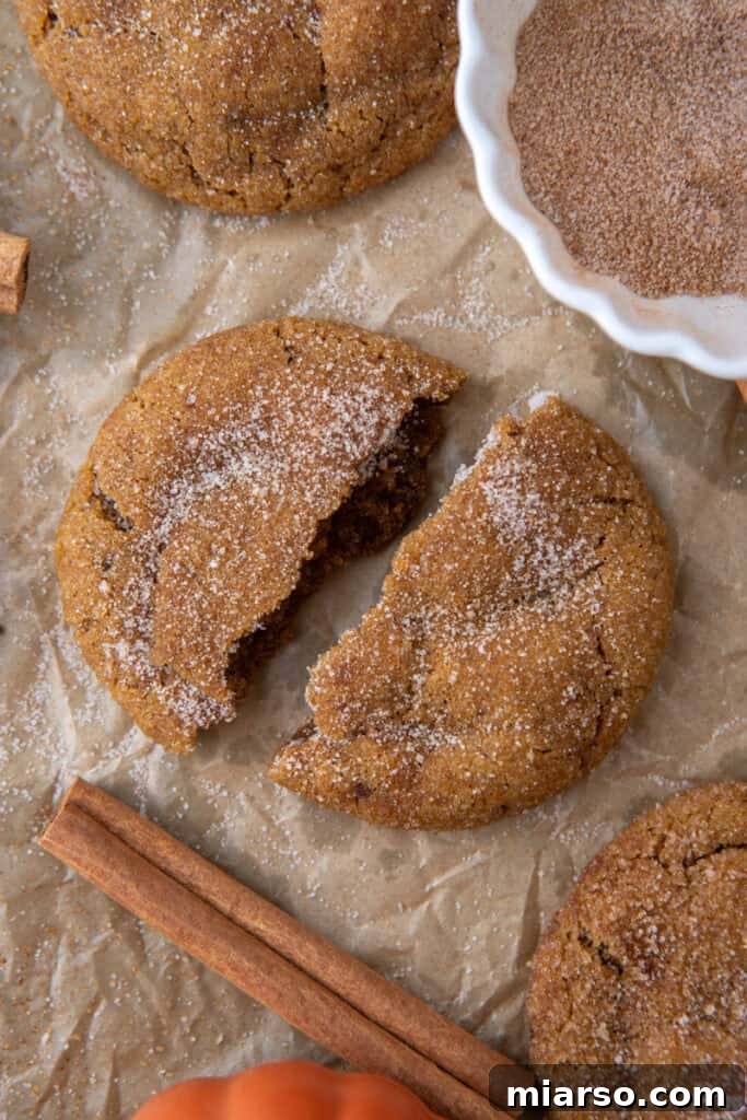 A Brown Butter Pumpkin Snickerdoodle Cookie split in half, revealing its soft, pumpkin-spiced interior
