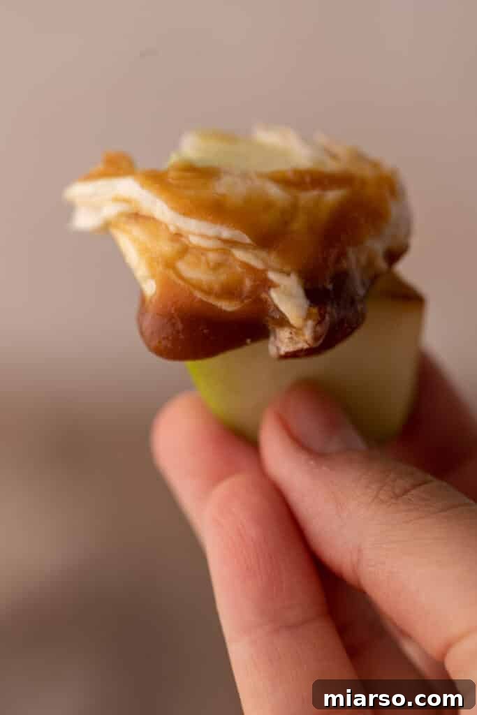 Close-up of an apple slice generously coated with creamy caramel cheesecake dip, ready to eat.
