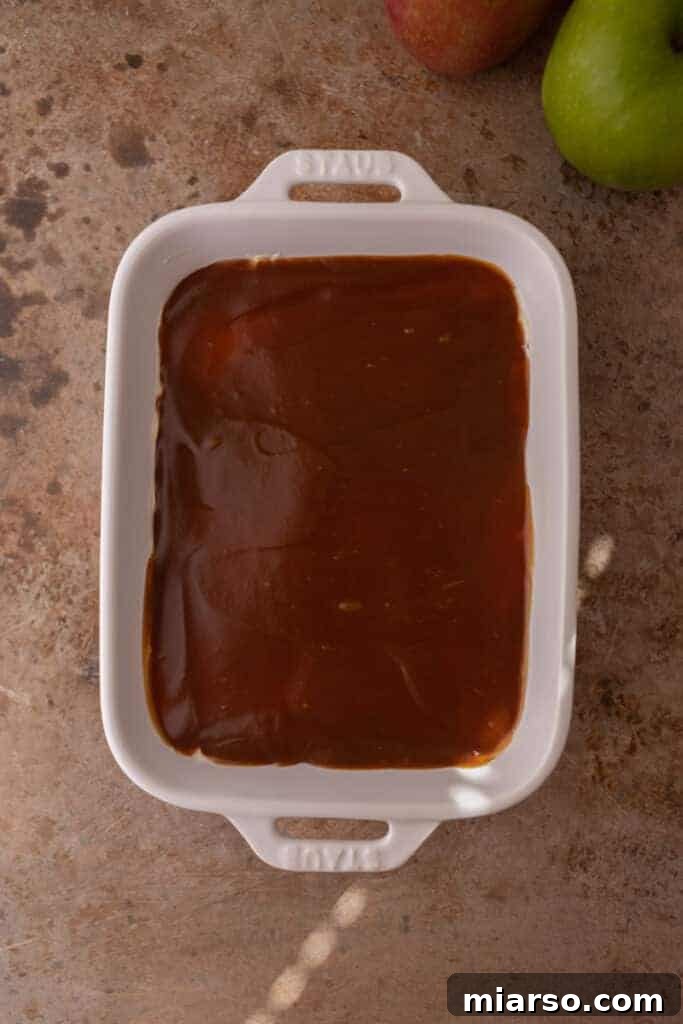 Rich caramel sauce being spread over the cheesecake layer, creating a delicious second tier.