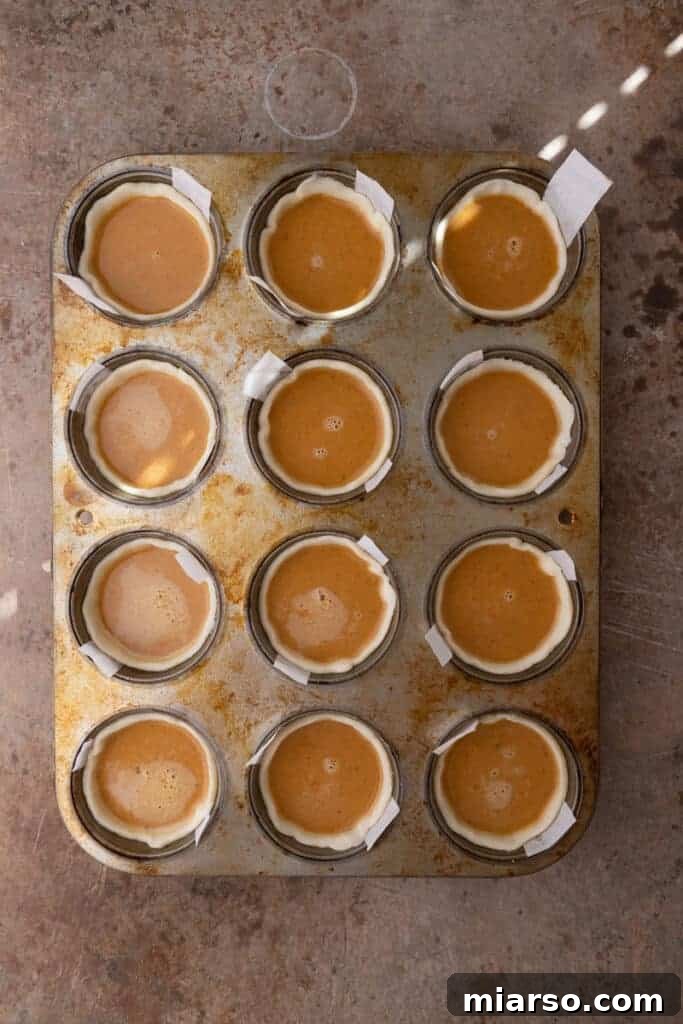 Bite-Sized Pumpkin Delights in a Muffin Tin 9 Raw dough and pumpkin batter in individual muffin tin cups, ready to be baked into mini pumpkin pies.