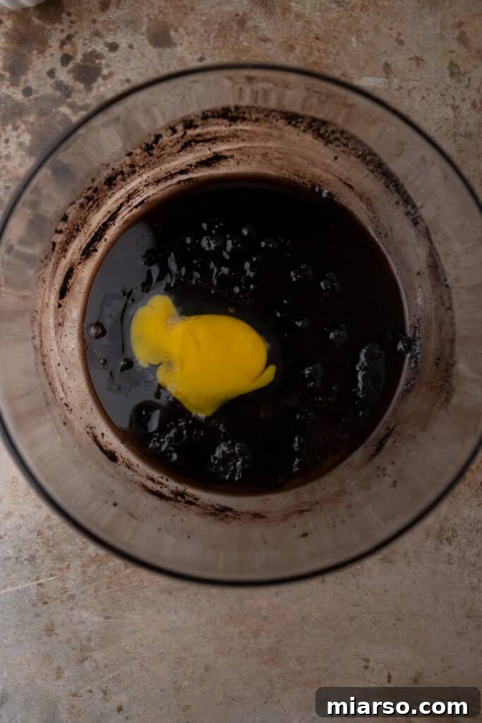 Dark cocoa batter in a bowl with an egg mixed in there