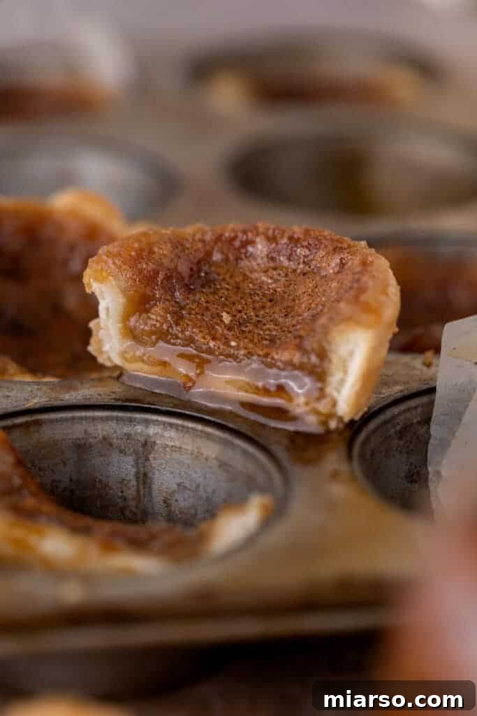 A Canadian butter tart neatly sliced in half, revealing its glistening, gooey caramel filling and flaky golden crust