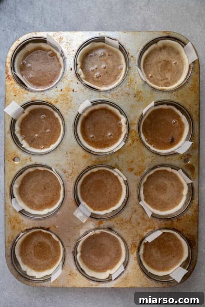 Unbaked Canadian butter tarts filled with gooey custard, placed in a muffin tin, ready for the oven