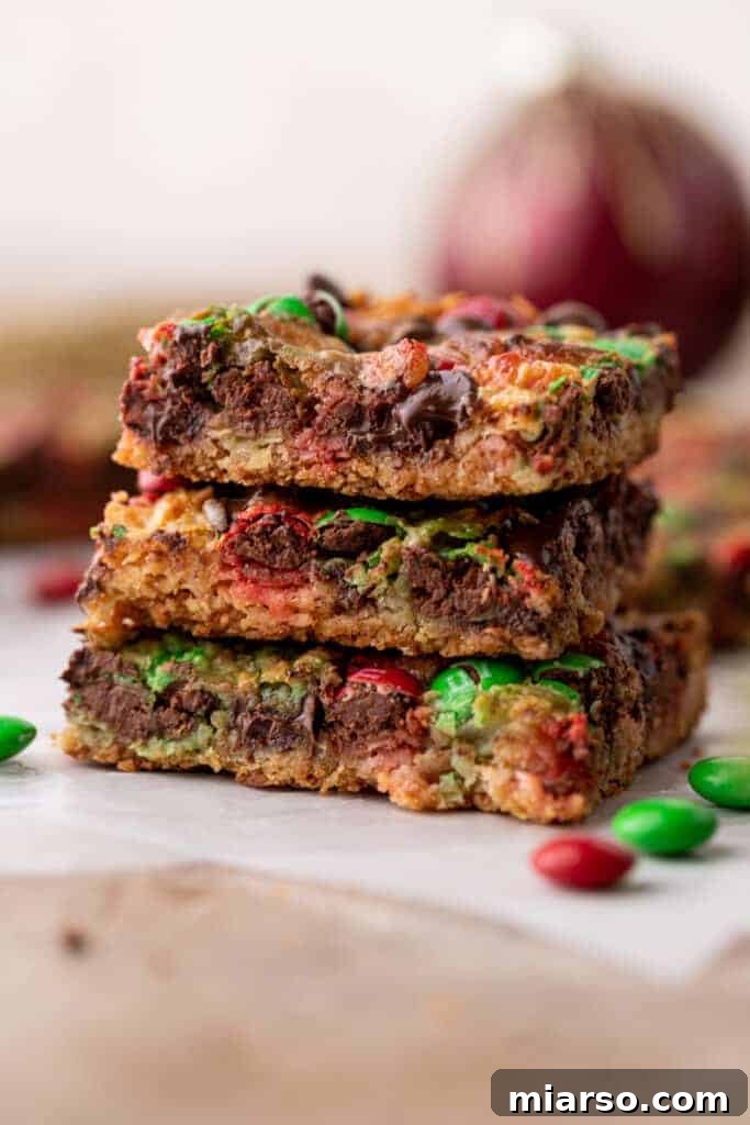 A stack of perfectly cut Christmas cookie bars, showcasing the distinct layers and colorful toppings