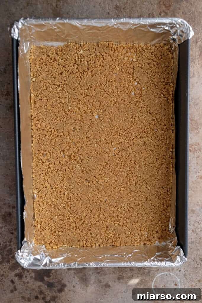 Graham cracker crust being pressed into a baking pan