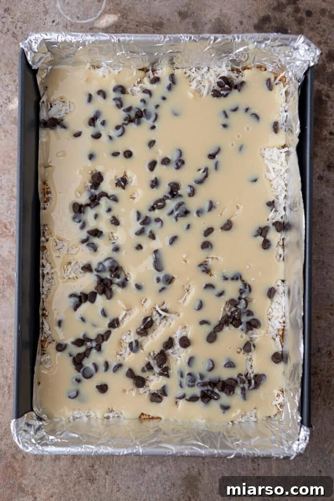 Sweetened condensed milk drizzled over the other ingredients of Christmas magic cookie bars