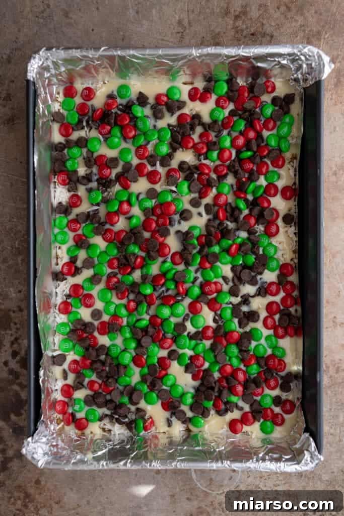 Unbaked Christmas magic cookie bars with M&Ms and chocolate chips in a pan, ready for the oven