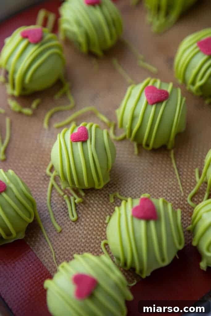 a bunch of rolled out green coated grinch oreo truffles laid out on a baking sheet
