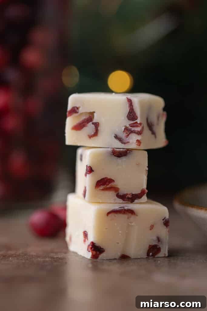Three squares of decadent Cranberry White Chocolate Fudge stacked, ready for holiday enjoyment.