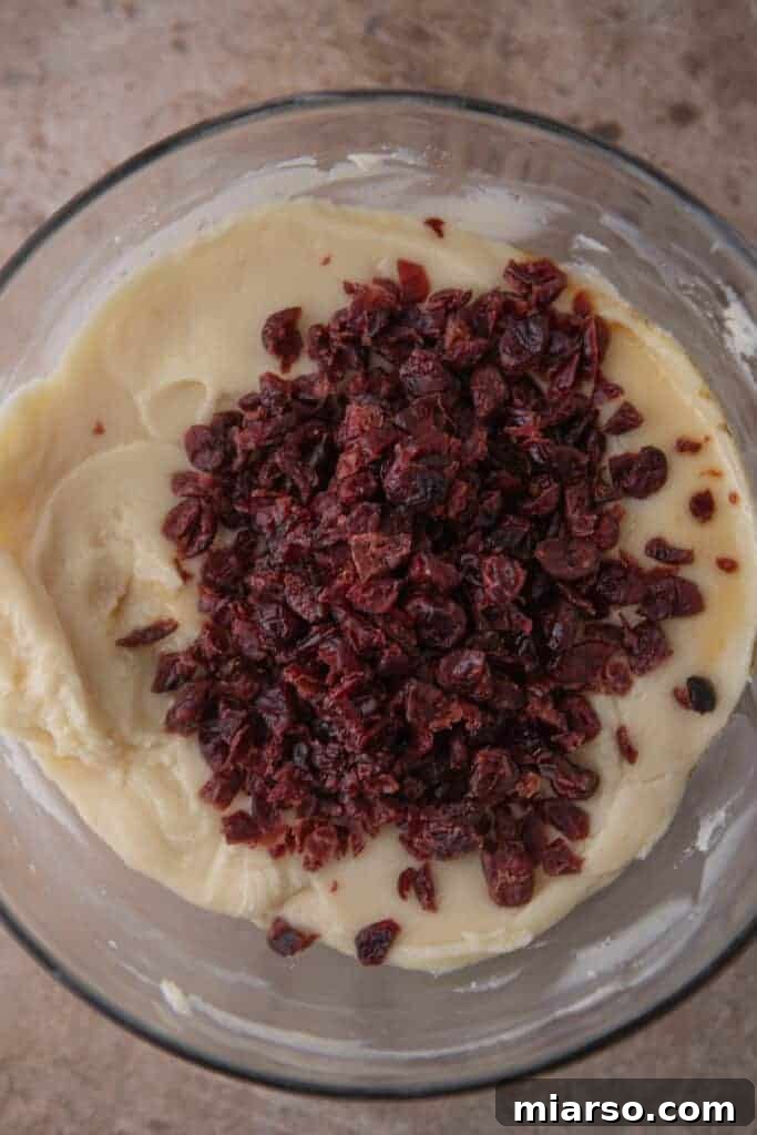 Dried cranberries being stirred into the melted white chocolate fudge mixture.
