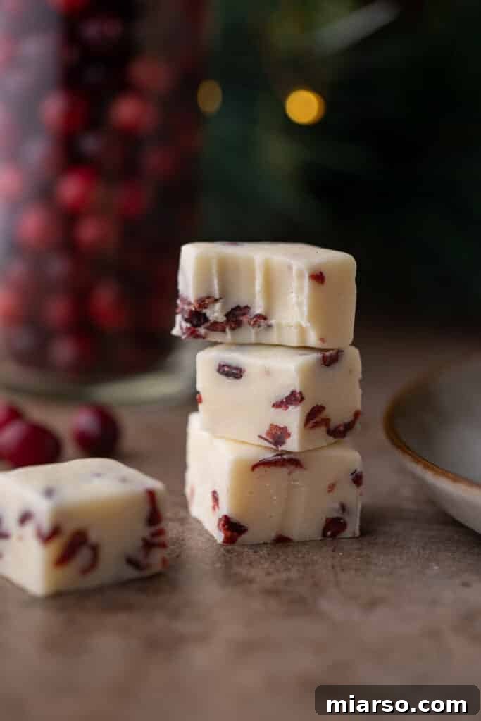 Three Cranberry White Chocolate Fudge squares stacked, with one showing a bite mark, highlighting its creamy texture.