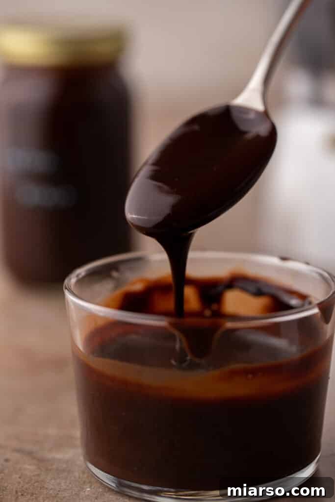 Ultimate Homemade Mocha Coffee Syrup 2 A spoon pouring rich, dark mocha coffee syrup into a cup, highlighting its thick and glossy texture.