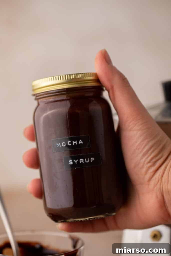 Ultimate Homemade Mocha Coffee Syrup 4 A hand holding up a mason jar filled with freshly made homemade mocha coffee syrup, showcasing its rich color.