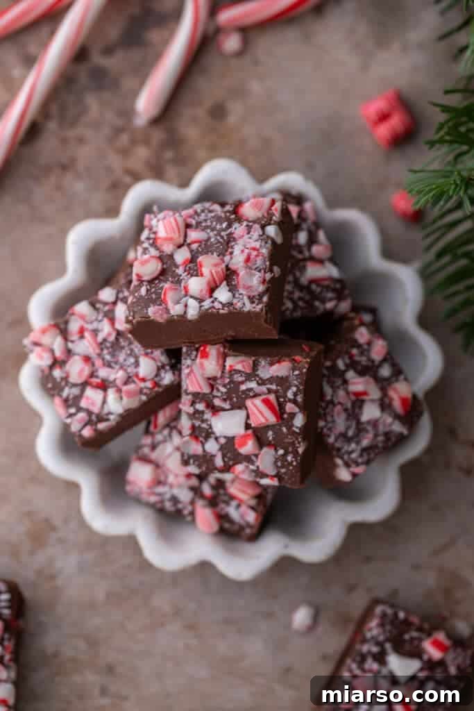 An overhead shot of multiple squares of peppermint fudge neatly stacked in a bowl, showing the crushed candy cane topping.