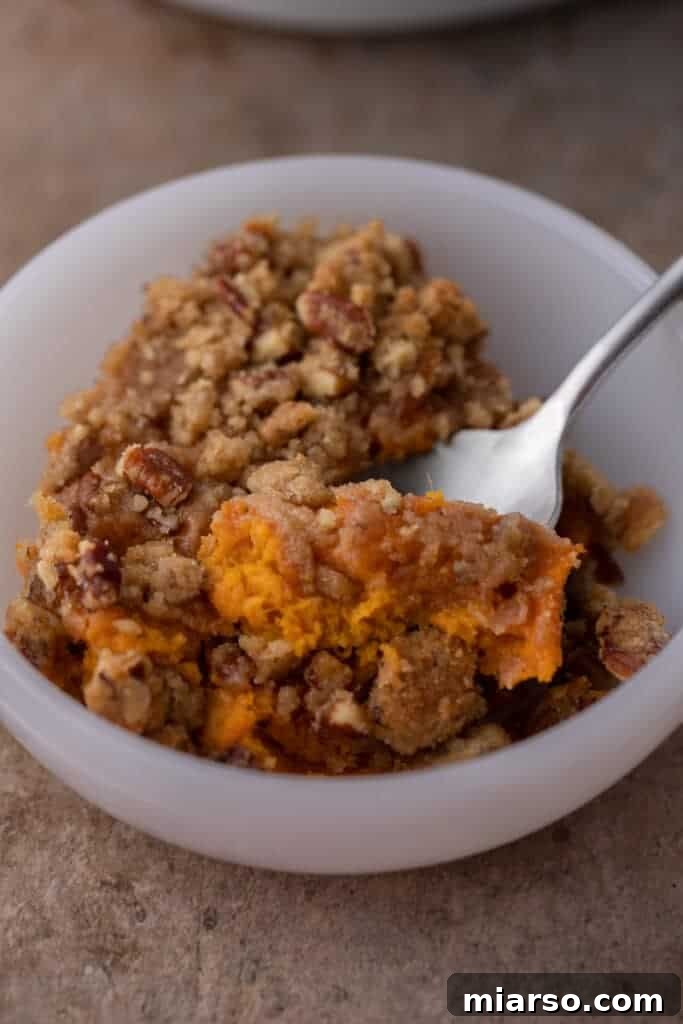 Pecan-Topped Sweet Potato Perfection 14 spoon in a bowl full of sweet potato casserole with pecan topping